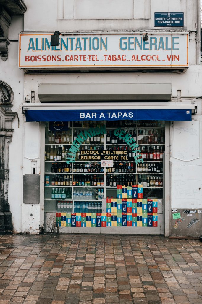 Street photography in Brussels on a rainy day – neighborhood grocery storefront with stacked drink crates