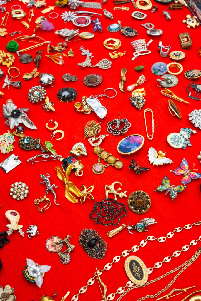 Collection of vintage brooches and pins arranged neatly on bright red cloth at a Brussels flea market.