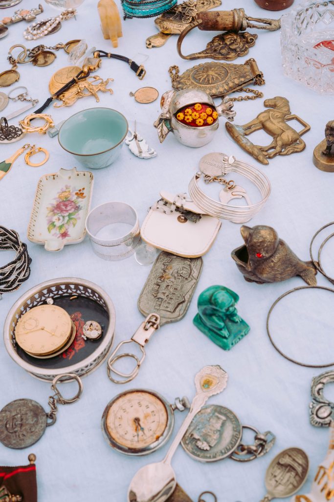 Antique objects including pocket watches, spoons and decorative metal pieces at a Brussels market stall.