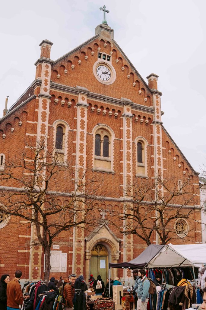 Brick church facade behind clothing stalls at Place du Jeu de Balle flea market in Brussels.