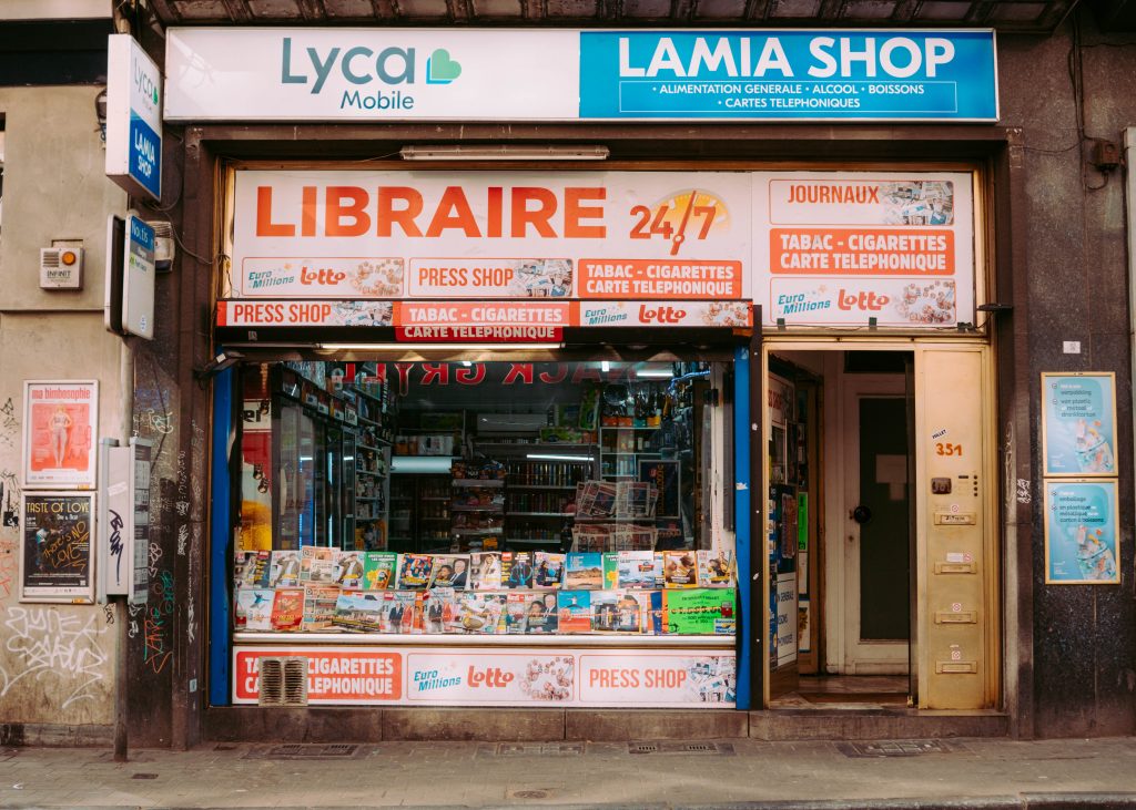 Street photography scene of a press shop storefront with newspapers and signage in Brussels