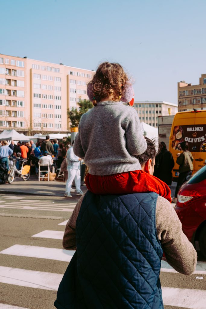 child sitting on father's shoulders at busy outdoor market in Ixelles Brussels